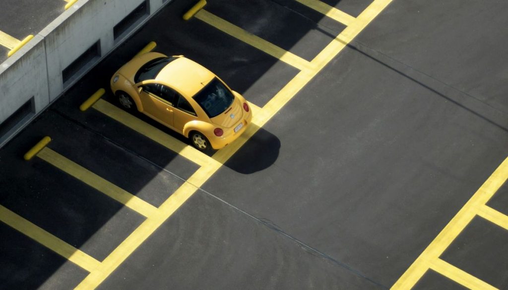 An overhead shot of a yellow VW Beetle parked in an empty car park.